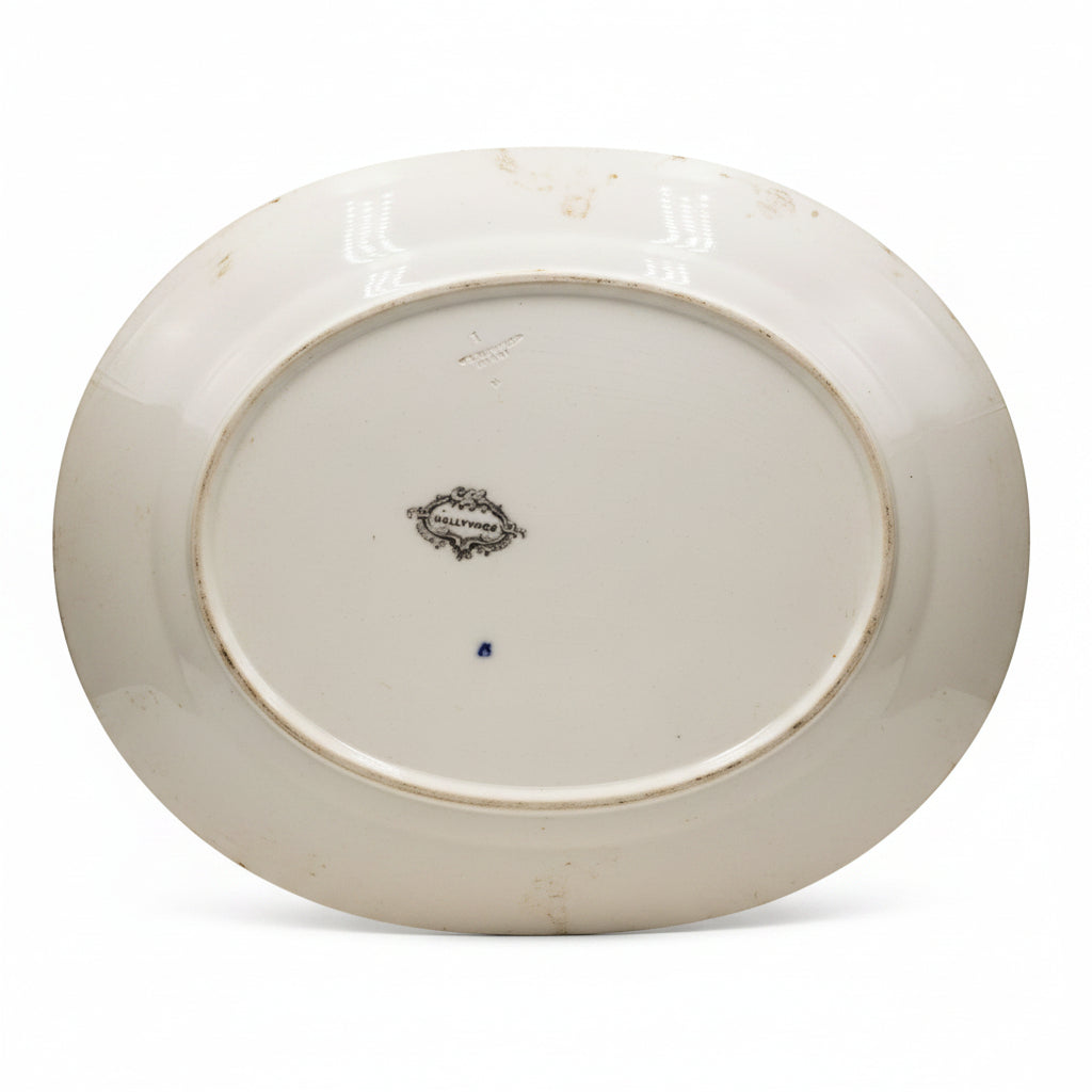 The underside of a white ceramic oval platter or serving dish, showing a small central maker's mark and a blue dot on the glazed surface.