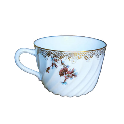 A white ceramic teacup with a gold decorative band and delicate floral illustrations, resting on a rustic wooden table.