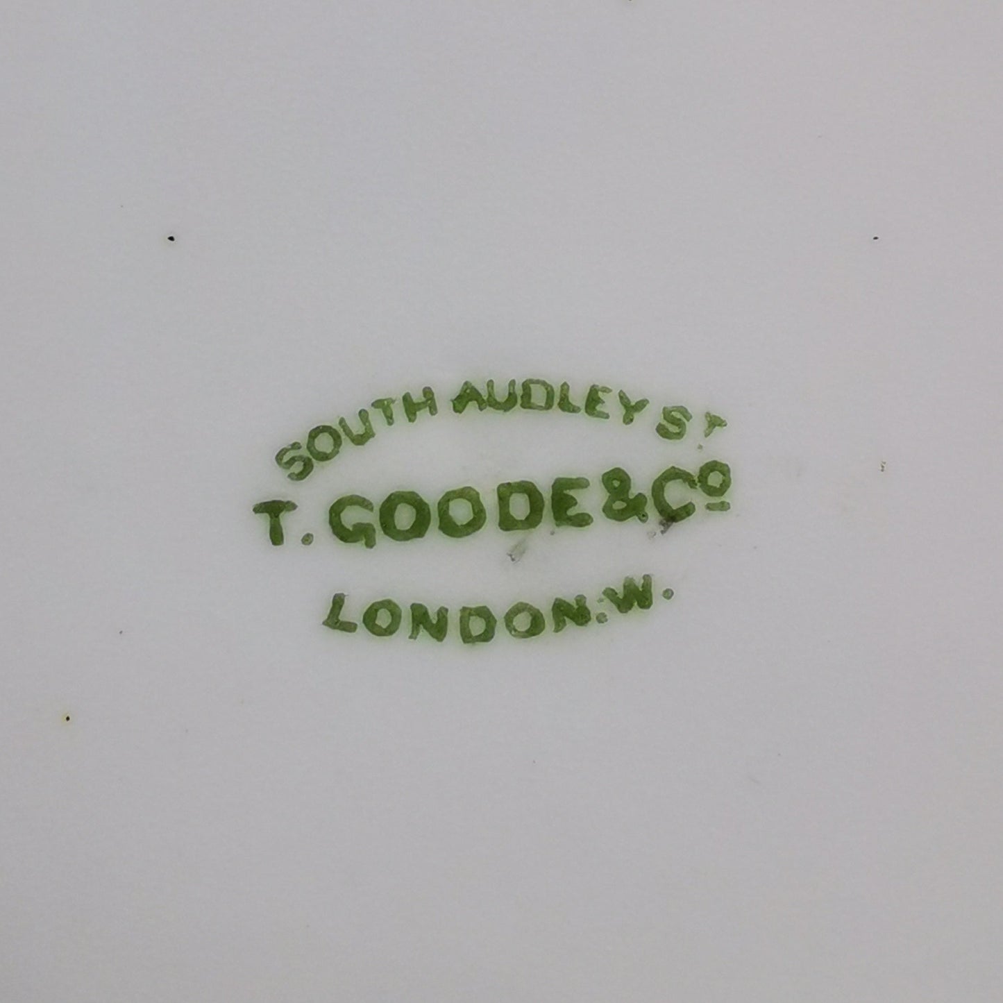Close-up of the bottom of a white porcelain dish or cup, showing green printed maker's mark text reading 'SOUTH AUDELY ST T. GOODE & Co LONDON' with some brown staining near the rim.