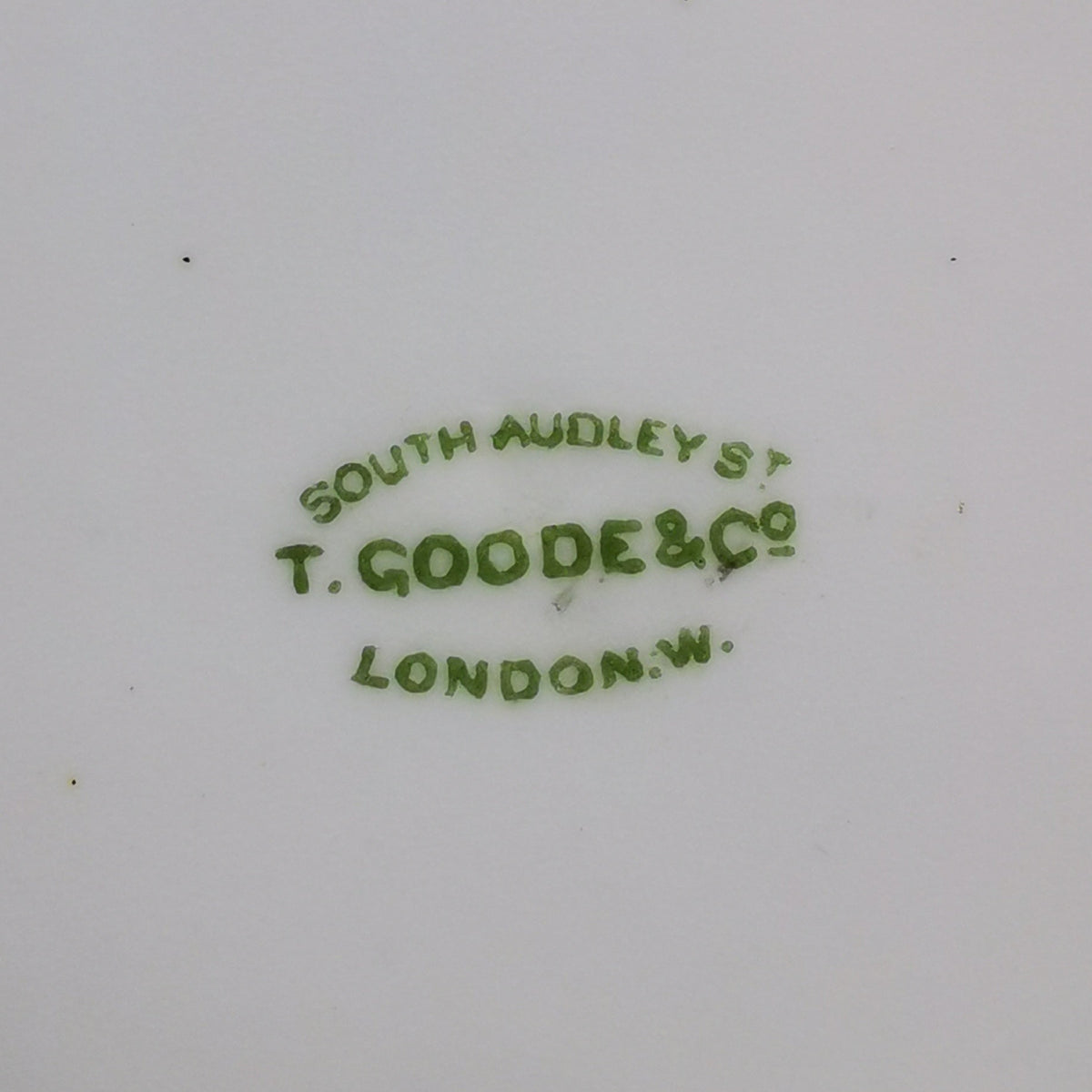 Close-up of the bottom of a white porcelain dish or cup, showing green printed maker's mark text reading 'SOUTH AUDELY ST T. GOODE & Co LONDON' with some brown staining near the rim.