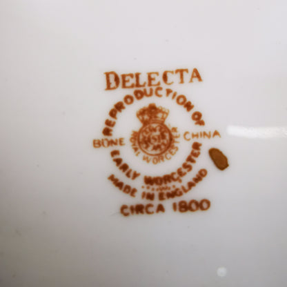 Close-up of a white ceramic surface printed with a brown reproduction mark reading 'DELECTA' and 'Reproduction of Early Worcester Made in England circa 1800' with a crest.