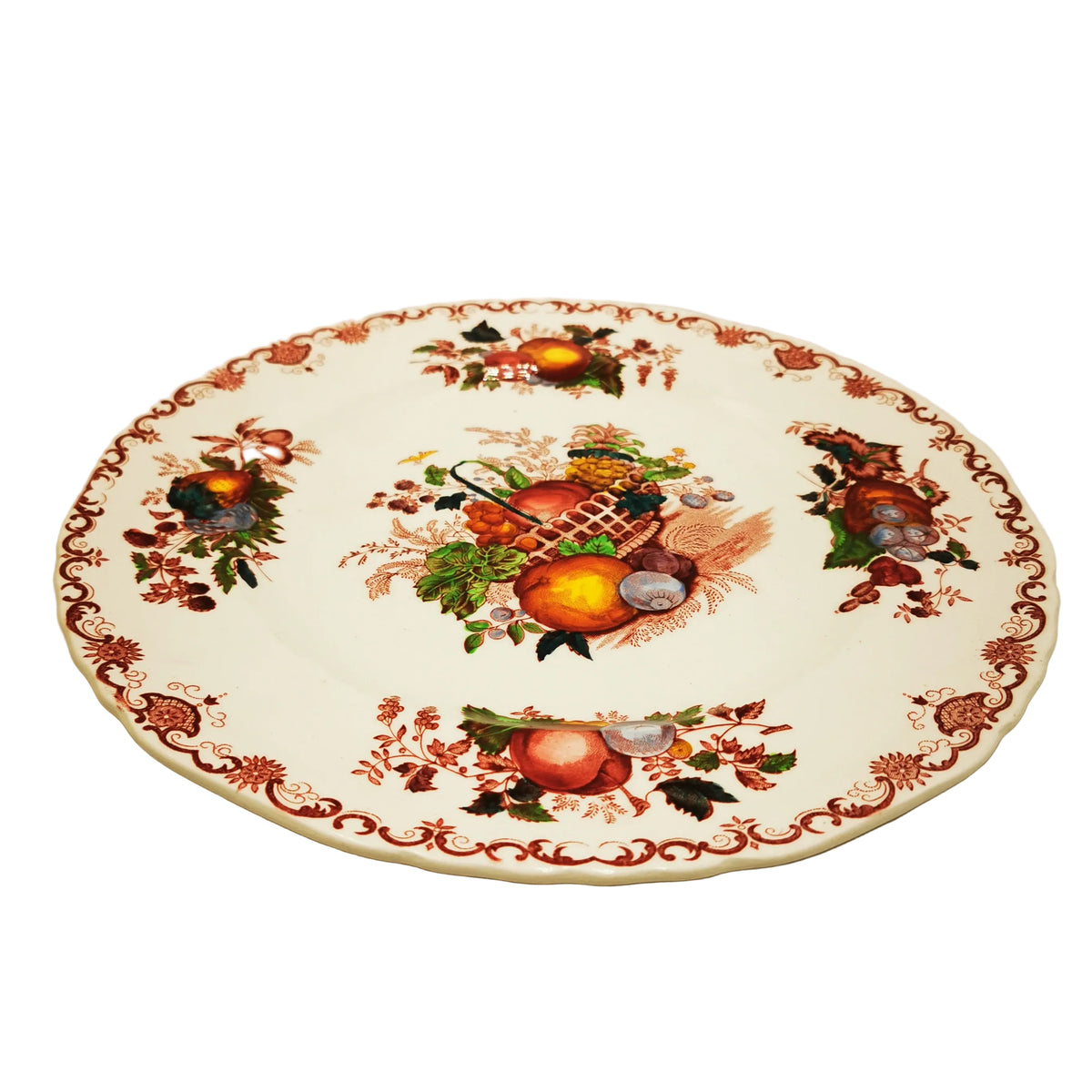 A vintage ceramic serving platter with a white base, decorated with a central fruit and vegetable motif and a red floral border, set against a plain beige background.