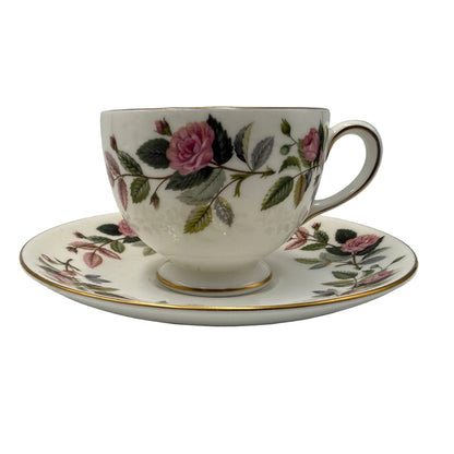A vintage white porcelain teacup and saucer set decorated with a pink rose and green leaf floral pattern, accented with gold trim.