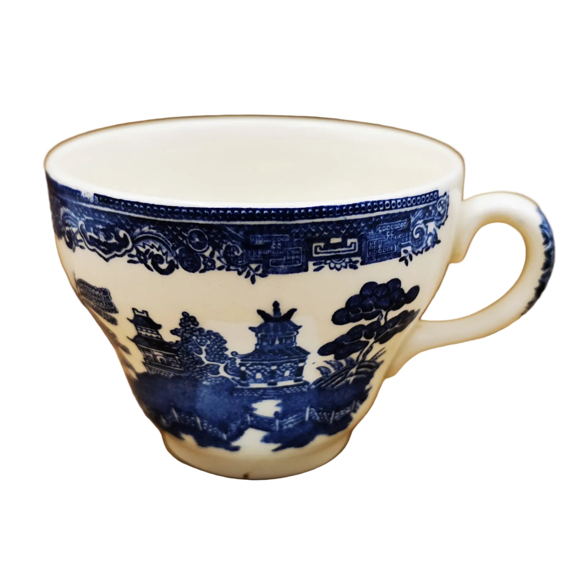 A white ceramic teacup with a classic blue underglaze landscape pattern, featuring pagodas, trees, and a decorative border, set against a brown cardboard background.