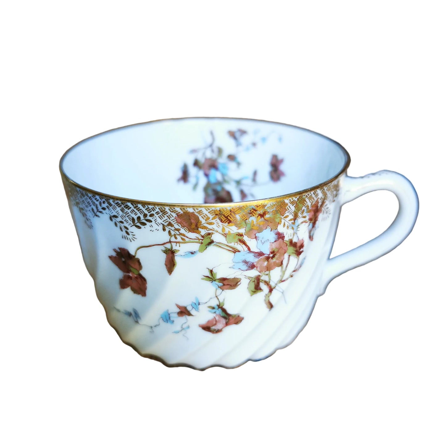 A white porcelain teacup with a delicate gold rim and a vintage floral pattern in brown, red, and blue, resting on a rustic wooden table.