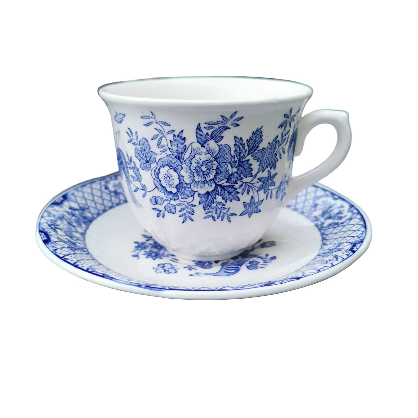 White teacup with blue floral pattern on a matching saucer, placed on a green surface with plants in the background.