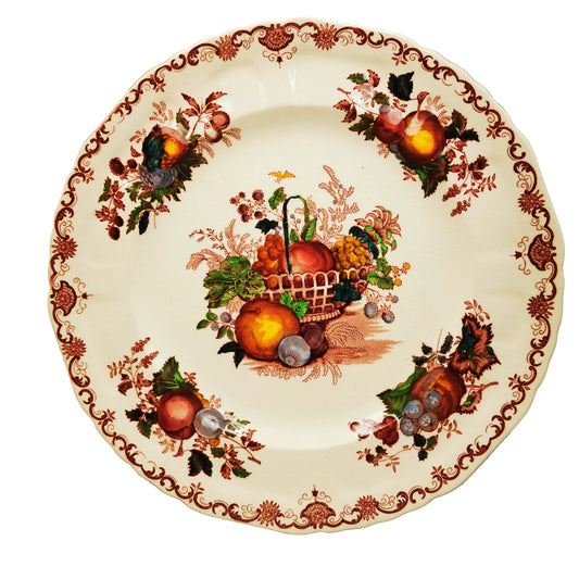 An antique ceramic plate with a white glaze, decorated with a brown floral scroll border and a central painted fruit and basket motif.