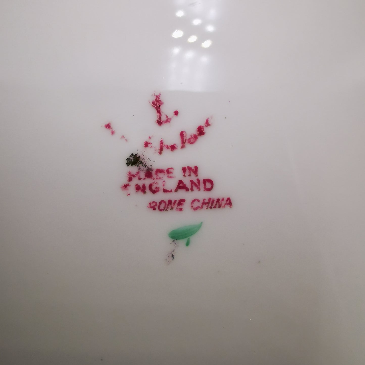 Close-up of the inside of a white ceramic plate or dish, showing red stamped text reading 'MADE IN ENGLAND' and 'GONE CHINA' along with a small green leaf mark.