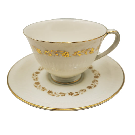 White teacup and saucer with gold floral patterns on a neutral background