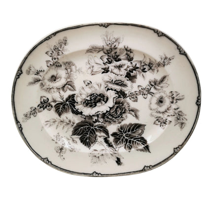 An oval white ceramic serving platter decorated with a black floral pattern of roses and leaves, featuring a decorative black border.