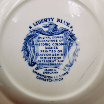 Close-up of the underside of a white ceramic dish or plate, showing blue printed text and crest reading 'LIBERTY BLUE' with colonial scene engraving details and 'MADE IN ENGLAND'.