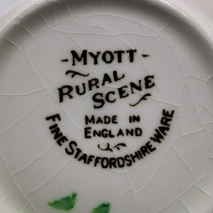 Close-up of the inside bottom of a white ceramic plate or dish with visible crackle glaze. Black printed text reads “MYOTT Rural Scene Made in England” and “FINE STAFFORDSHIRE WARE,” with a few small green marks near the bottom edge.
