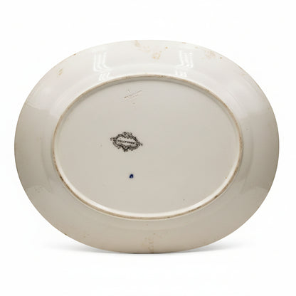 The underside of a white ceramic oval platter or serving dish, showing a small central maker's mark and a blue dot on the glazed surface.